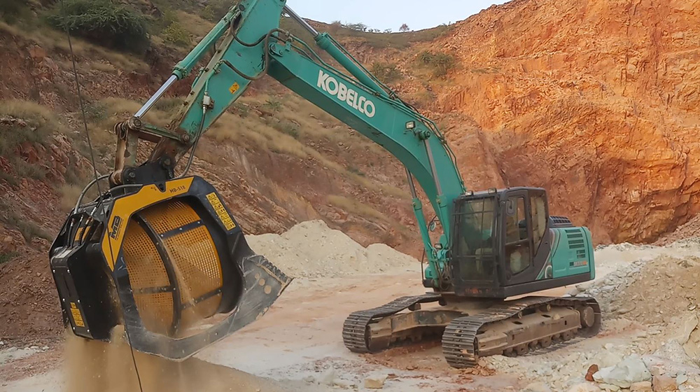 An MB Crusher MB-S18 screening bucket attached to a Kobelco SK220SD excavator screening sandstone in an Indian quarry