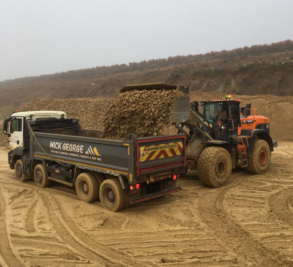A Doosan DL-7 series wheeled loader filling up a Mick George Group truck with quarry-processed material